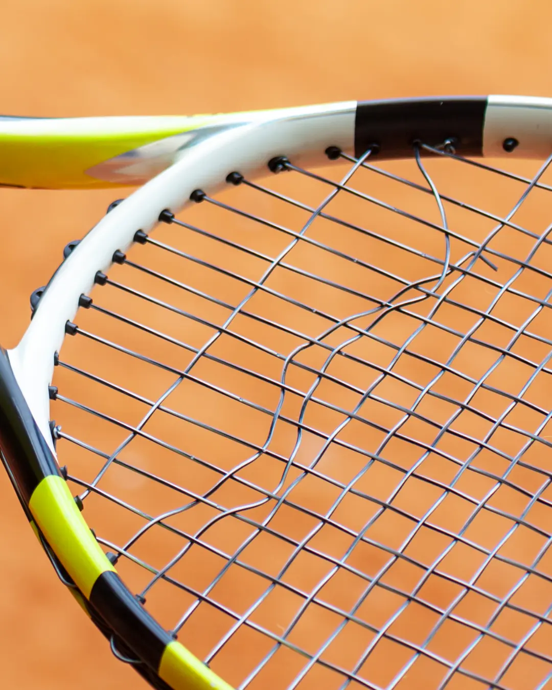 Dettaglio di una racchetta da tennis con corde rotte e usurate su campo in terra battuta, simbolo di perdita di tensione e prestazioni.